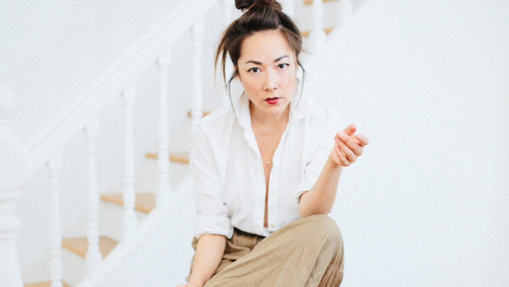 Woman sits on stool and leans forward.